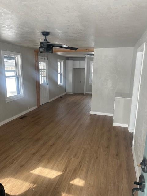 unfurnished living room with dark wood-type flooring, baseboards, and ceiling fan