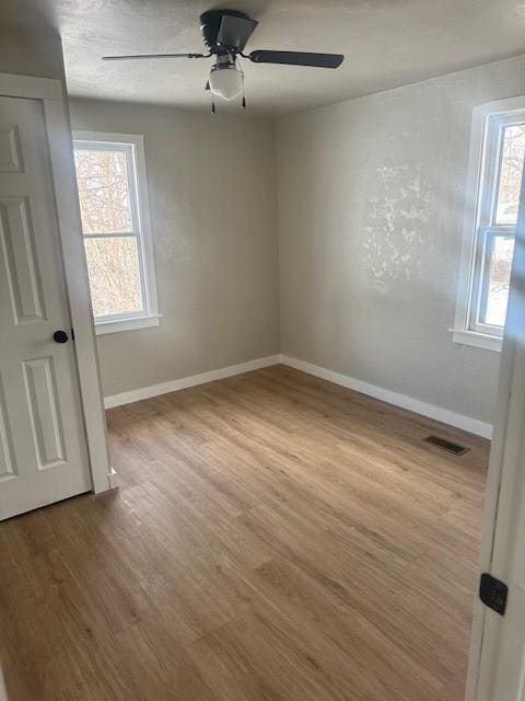 unfurnished room with a wealth of natural light, visible vents, baseboards, and wood finished floors