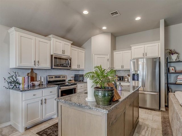 kitchen featuring a kitchen island with sink, white cabinetry, stainless steel appliances, stone counters, and lofted ceiling