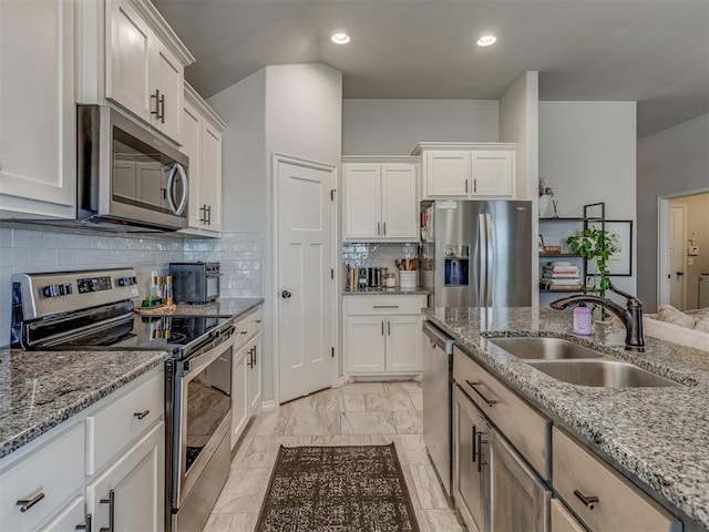 kitchen with a sink, stainless steel appliances, light stone counters, and white cabinets