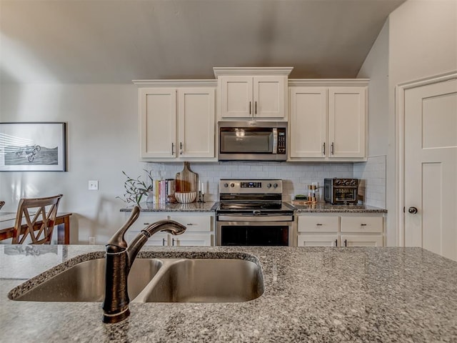 kitchen with light stone countertops, a sink, white cabinets, appliances with stainless steel finishes, and backsplash