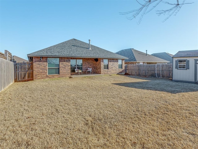 rear view of property featuring brick siding, a shingled roof, a fenced backyard, a yard, and an outbuilding