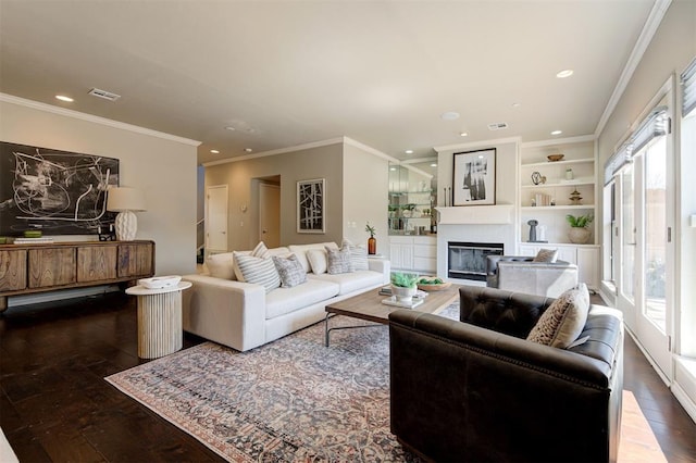 living area with visible vents, ornamental molding, a glass covered fireplace, and hardwood / wood-style floors