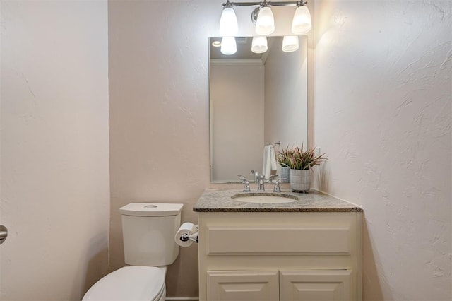 half bath featuring toilet, vanity, and a textured wall