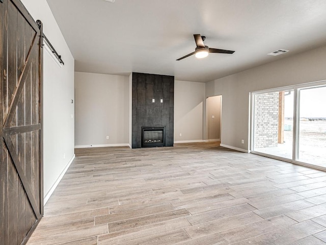 unfurnished living room featuring visible vents, ceiling fan, a tiled fireplace, light wood-type flooring, and a barn door