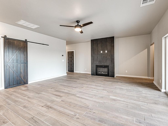 unfurnished living room with light wood-type flooring, visible vents, a barn door, and a fireplace