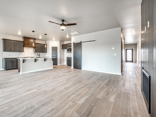 kitchen featuring a sink, stainless steel microwave, a barn door, light wood finished floors, and ceiling fan