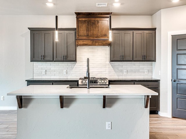 kitchen with a breakfast bar area, baseboards, visible vents, light wood finished floors, and tasteful backsplash