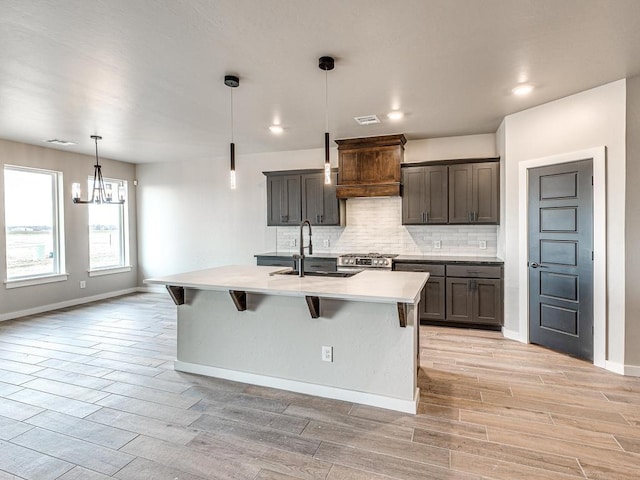 kitchen with wood tiled floor, stainless steel range with gas stovetop, decorative backsplash, custom exhaust hood, and a sink