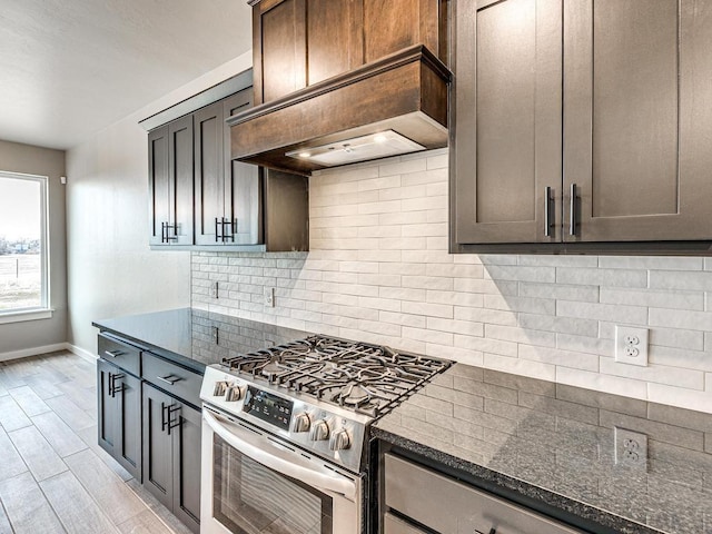 kitchen featuring stainless steel gas range oven, tasteful backsplash, dark stone countertops, light wood-style flooring, and custom exhaust hood