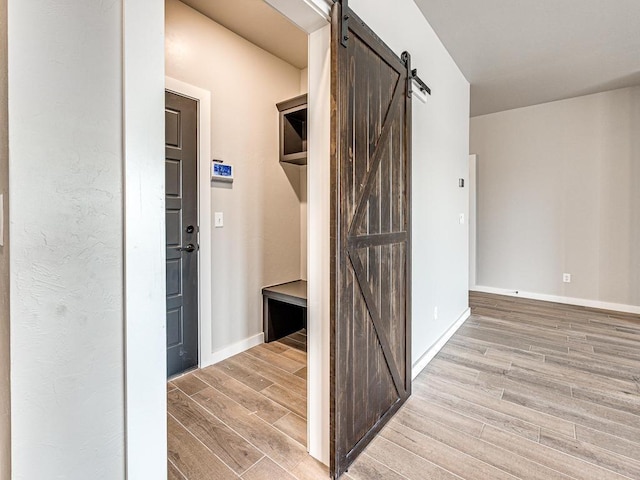 corridor featuring a barn door, baseboards, and light wood-style flooring