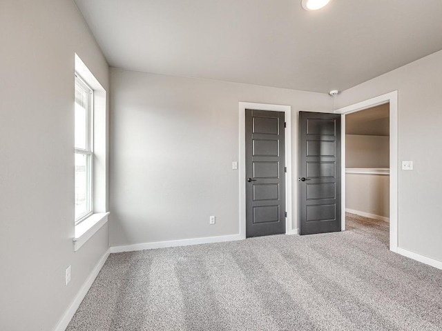 unfurnished bedroom with baseboards, multiple windows, a walk in closet, and carpet flooring