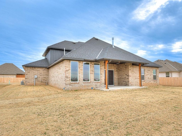 rear view of house featuring a patio, brick siding, roof with shingles, and fence