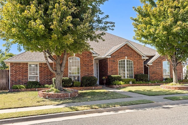 view of front facade with brick siding, a shingled roof, a front yard, and fence