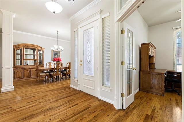 entryway featuring ornamental molding, wood finished floors, baseboards, a chandelier, and ornate columns