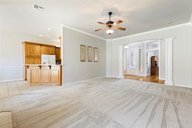 unfurnished living room featuring a ceiling fan, visible vents, ornate columns, ornamental molding, and light colored carpet