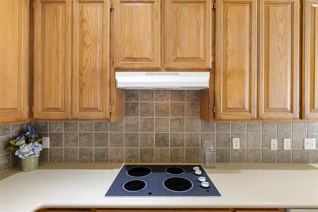 kitchen with decorative backsplash, light countertops, black electric cooktop, and under cabinet range hood