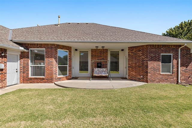 rear view of house with a patio area, brick siding, a yard, and roof with shingles