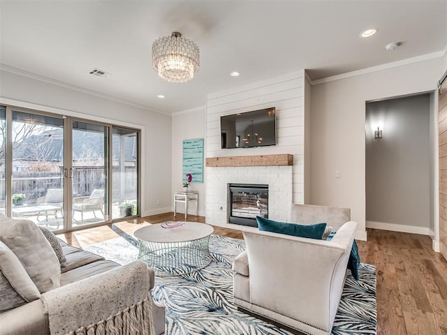 living area with wood finished floors, visible vents, baseboards, a fireplace, and crown molding