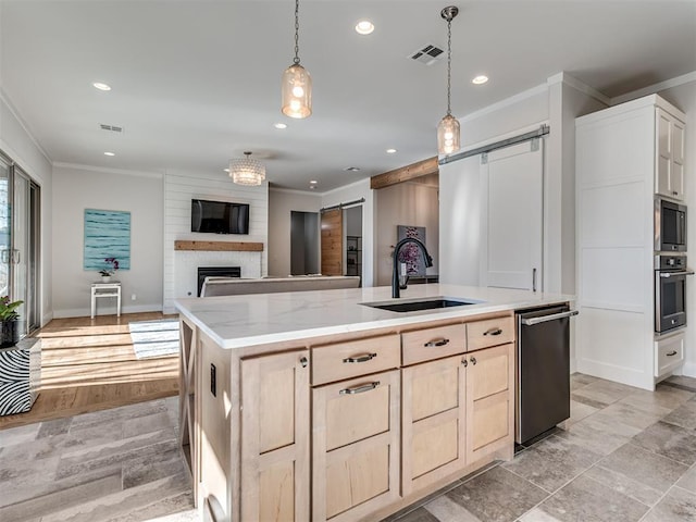 kitchen with light brown cabinetry, stainless steel appliances, a barn door, and a sink