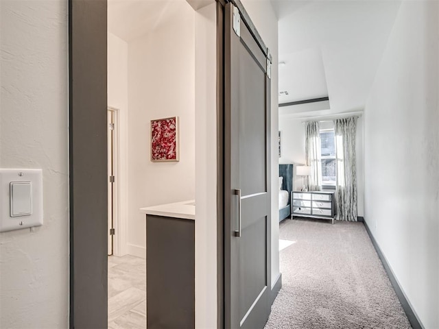 hall with a barn door, baseboards, and light carpet