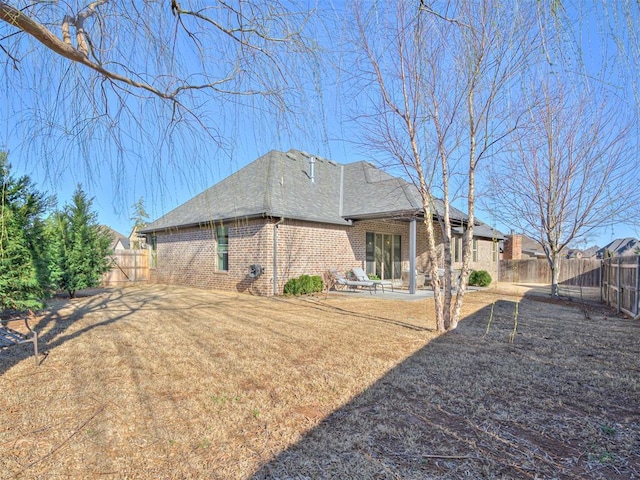 rear view of house with brick siding, roof with shingles, a fenced backyard, and a patio area