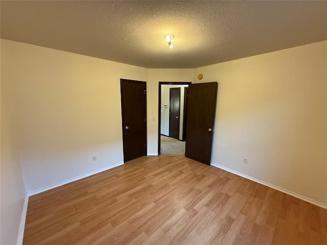 empty room featuring baseboards, light wood finished floors, and a textured ceiling