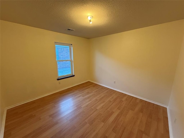 spare room featuring visible vents, baseboards, a textured ceiling, and wood finished floors