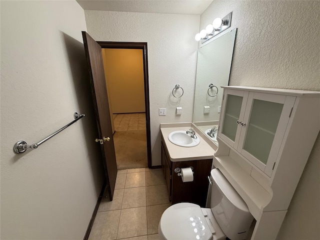 half bath with tile patterned floors, toilet, vanity, and a textured wall