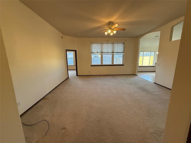 spare room with arched walkways, light colored carpet, baseboards, and a ceiling fan