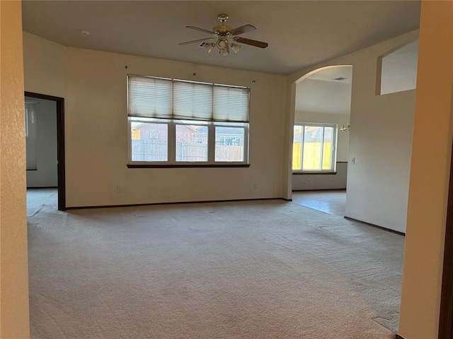 carpeted empty room with baseboards, arched walkways, and ceiling fan