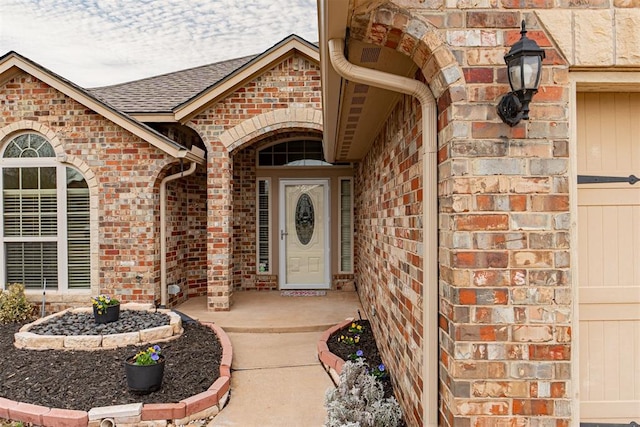 entrance to property featuring brick siding and a shingled roof