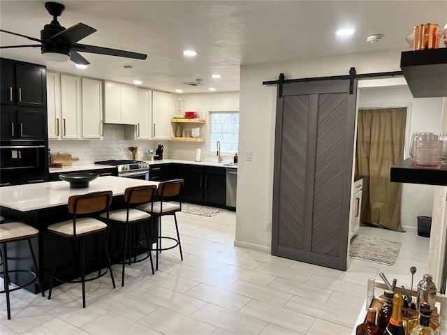 kitchen featuring open shelves, light countertops, appliances with stainless steel finishes, a barn door, and dark cabinets