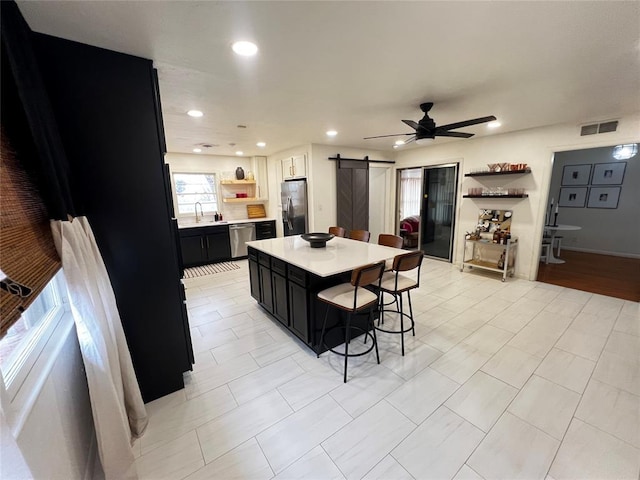 kitchen featuring open shelves, light countertops, appliances with stainless steel finishes, a barn door, and dark cabinets