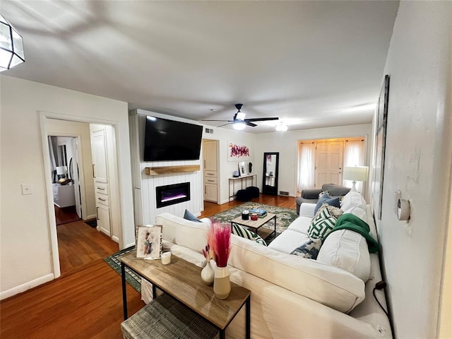 living room featuring visible vents, baseboards, ceiling fan, wood finished floors, and a glass covered fireplace