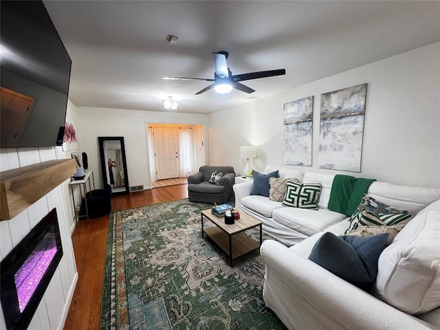 living area with ceiling fan, visible vents, wood finished floors, and a tile fireplace