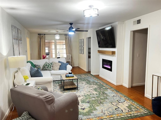 living area with visible vents, a glass covered fireplace, wood finished floors, baseboards, and ceiling fan