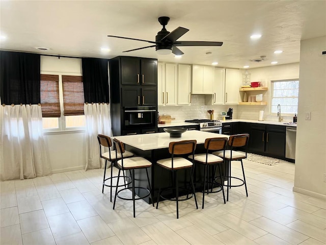 kitchen featuring backsplash, open shelves, dark cabinetry, stainless steel appliances, and a sink