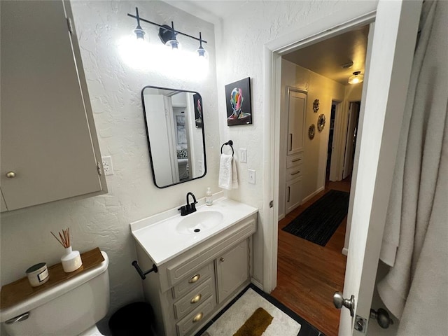 half bath featuring toilet, wood finished floors, vanity, and a textured wall