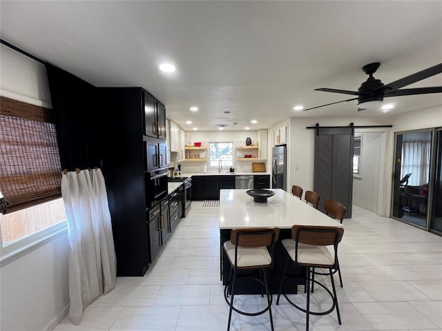 kitchen featuring open shelves, a barn door, stainless steel appliances, light countertops, and dark cabinets