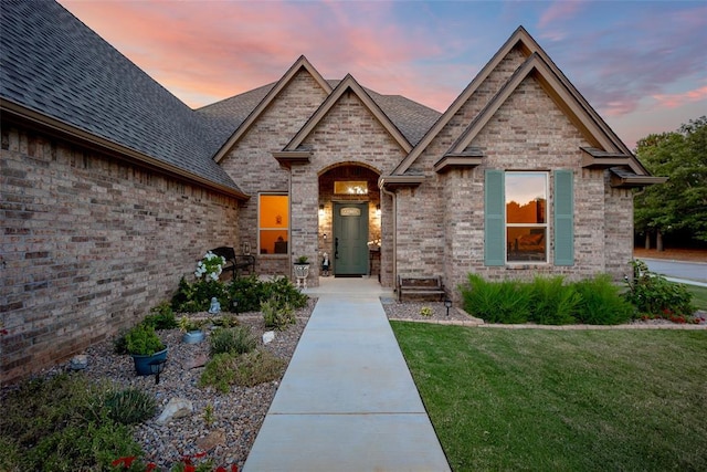 french country style house with brick siding, a shingled roof, and a front yard