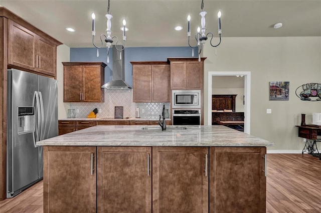 kitchen with light wood finished floors, a sink, stainless steel appliances, wall chimney exhaust hood, and tasteful backsplash