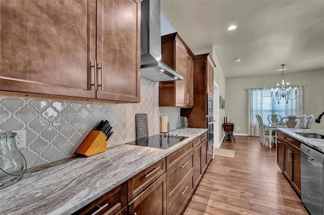 kitchen with light wood-style flooring, light stone counters, tasteful backsplash, stainless steel appliances, and wall chimney exhaust hood