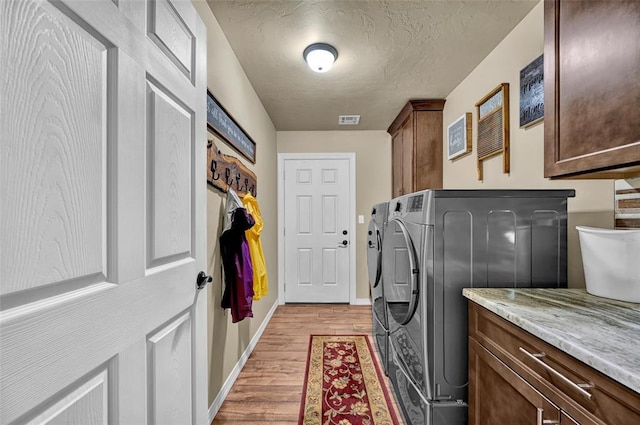 washroom featuring visible vents, washer and dryer, light wood-style floors, cabinet space, and a textured ceiling