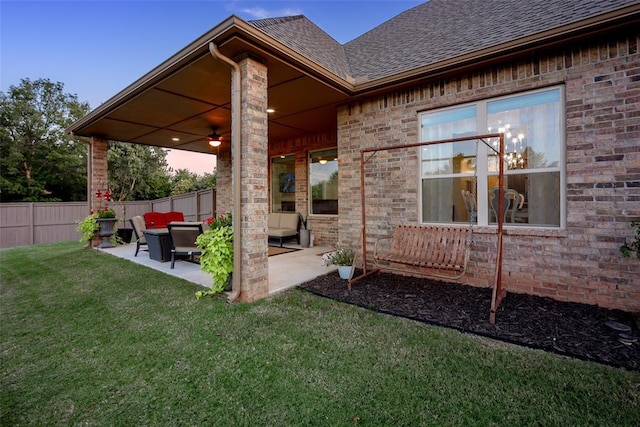 exterior space featuring fence, a yard, a shingled roof, brick siding, and a patio area