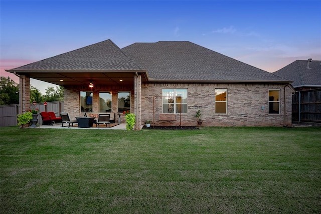 back of house at dusk with a yard, fence, roof with shingles, and a patio area