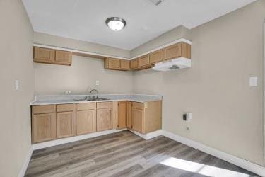 kitchen with a sink, baseboards, wood finished floors, and light countertops