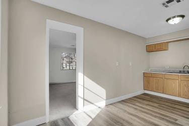 kitchen featuring visible vents, a sink, wood finished floors, light countertops, and baseboards