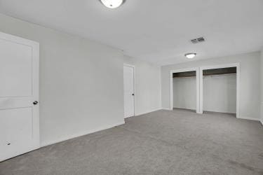 unfurnished bedroom with visible vents, two closets, and carpet flooring