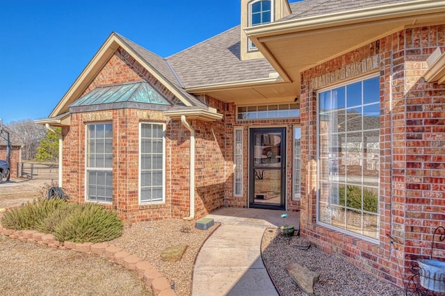 property entrance featuring brick siding and a shingled roof